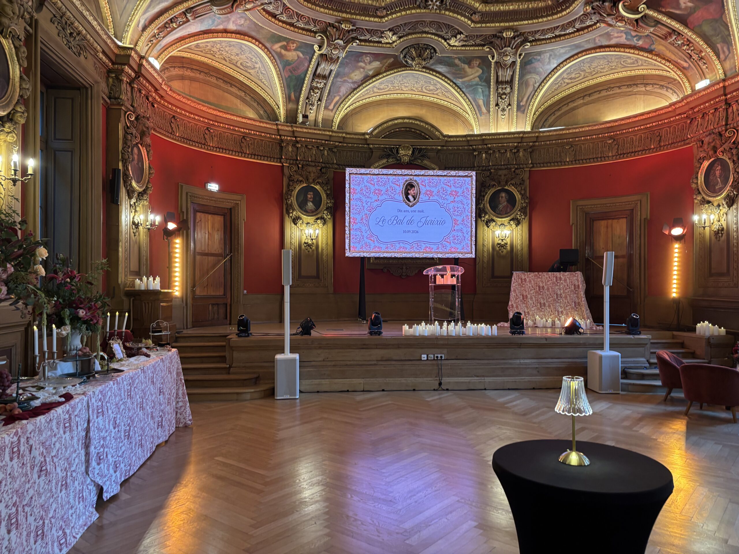 Salle de réception aux murs rouges et aux plafonds dorés, préparée pour le Bal de Jurixio.